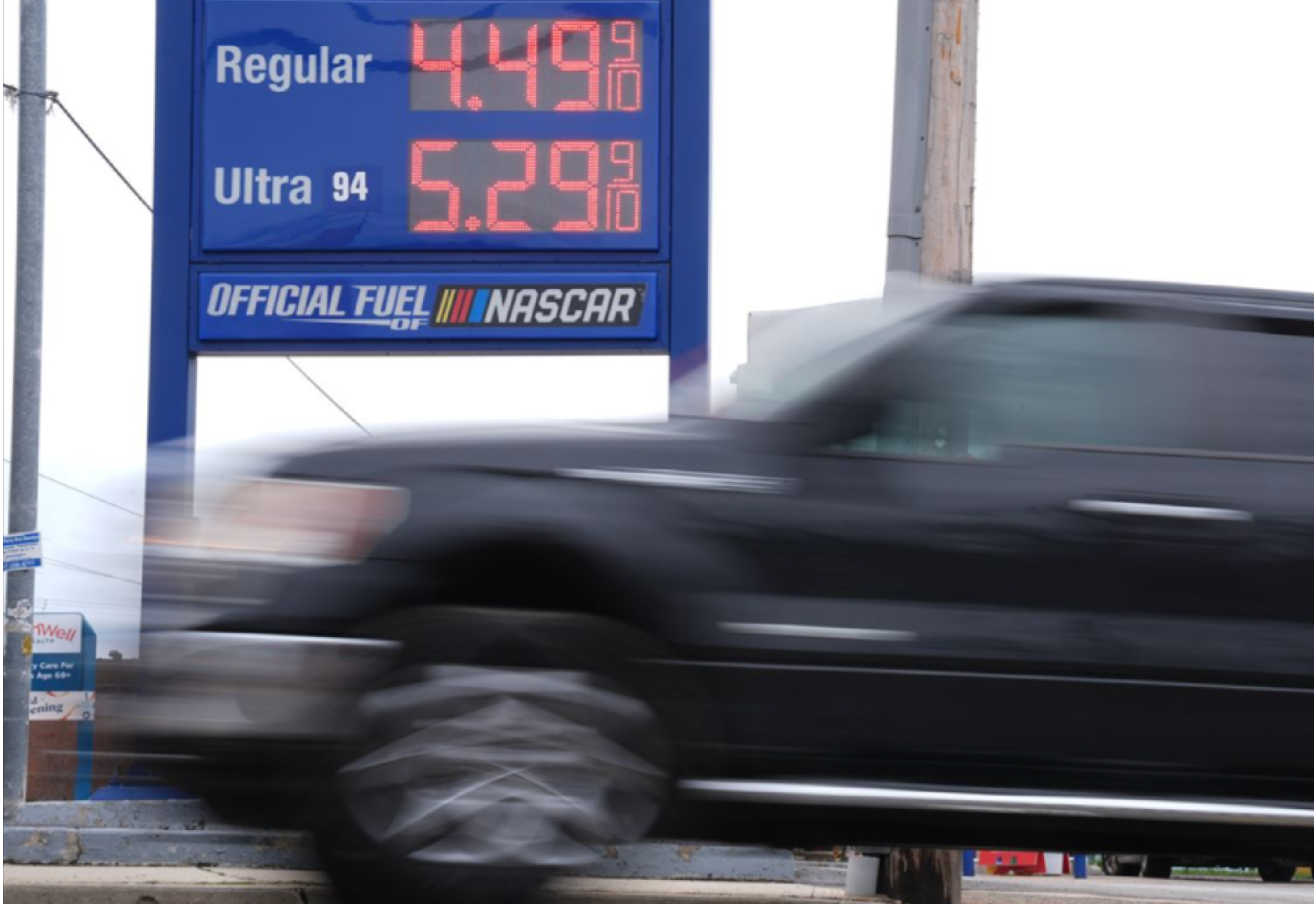 Gas station sign showing high fuel prices as cars pass by.